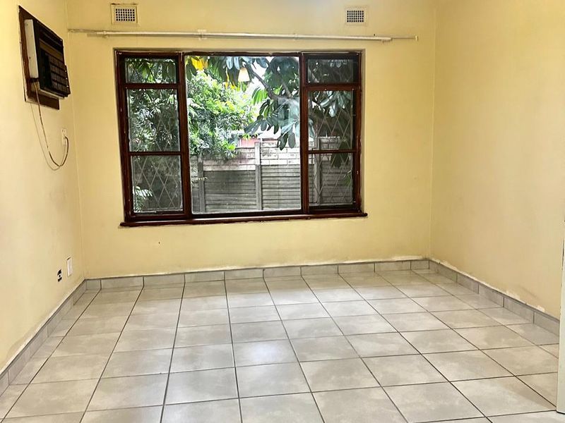 An empty living room featuring tiled flooring, a timber-framed window, and a built-in air conditioning unit, ready for personalization.