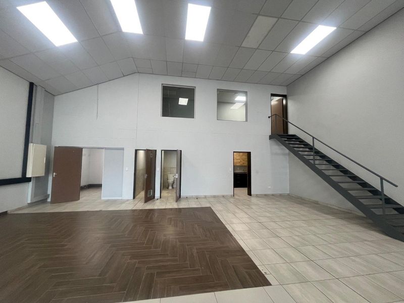 Spacious open-plan commercial area featuring a mix of wood-look and tiled flooring, a metal staircase, and high ceilings with recessed lighting.