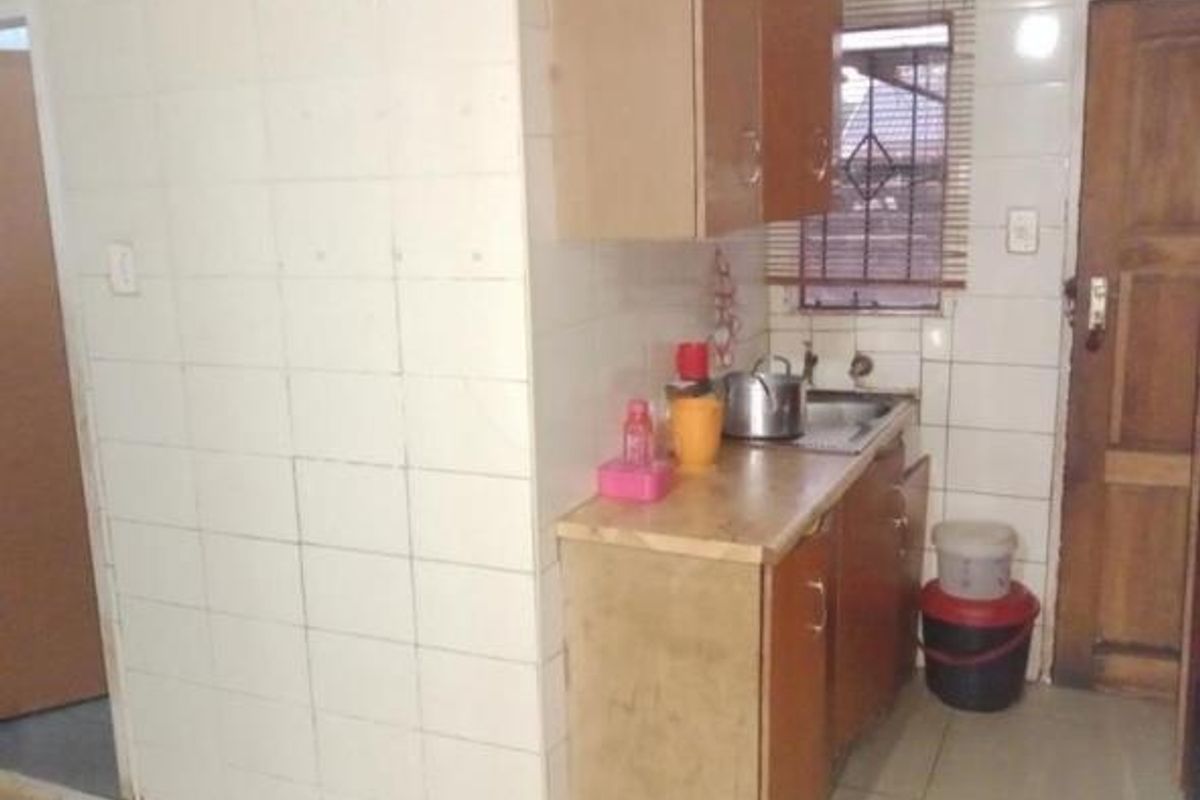 A compact kitchen area featuring tiled walls, wooden cabinetry, and a stainless steel sink, requiring cosmetic updates to modernize the space.