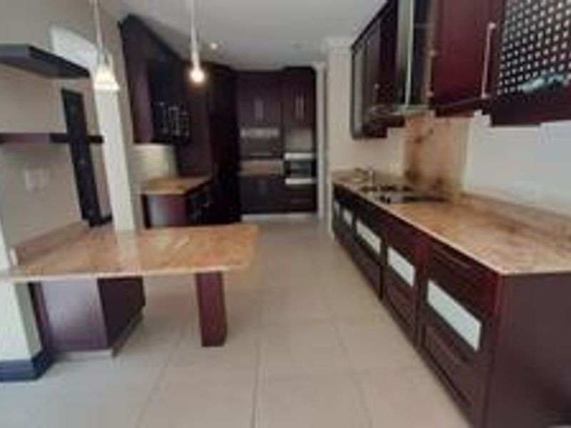 Spacious kitchen featuring dark wood cabinetry, stone countertops, integrated appliances, and a breakfast bar area with tiled flooring.