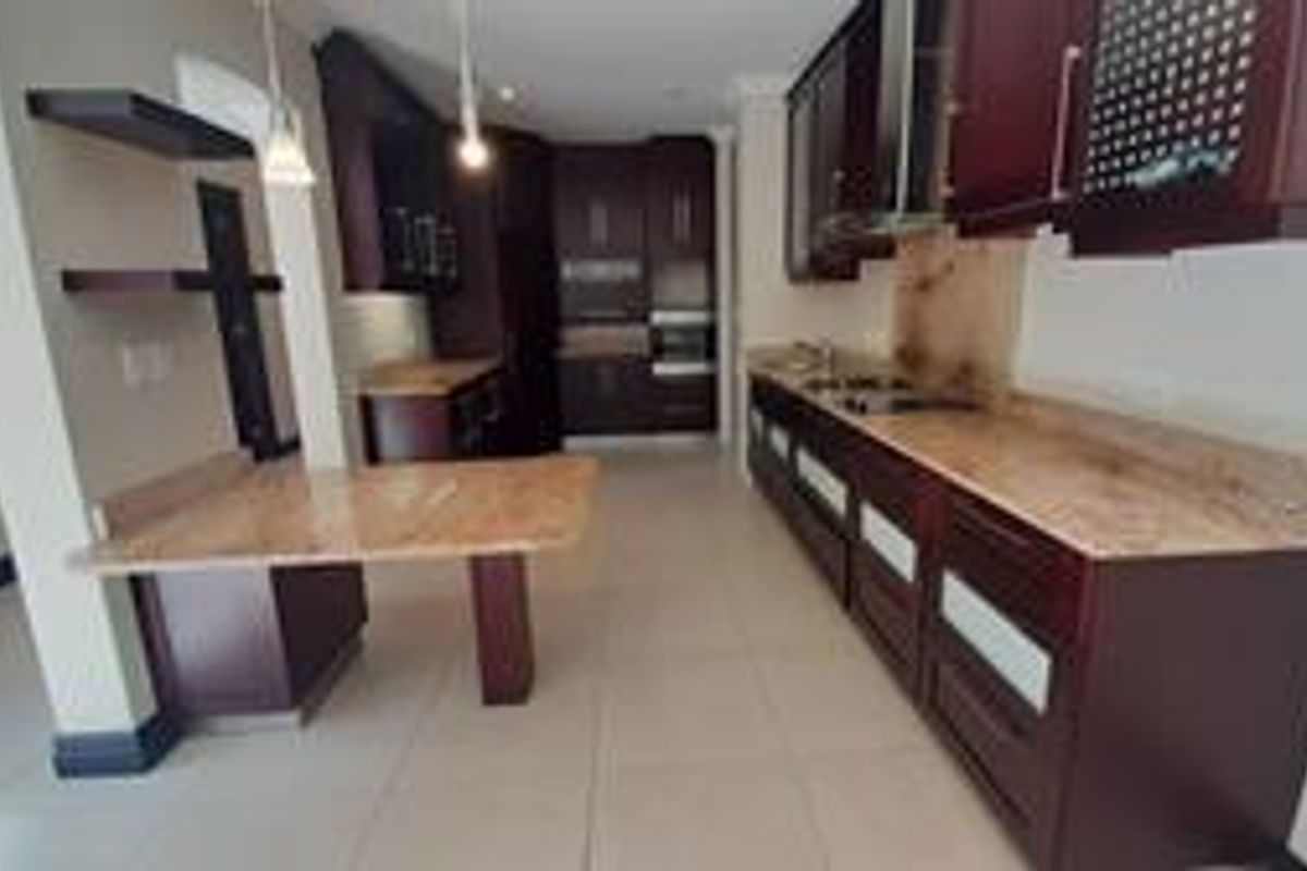 Spacious kitchen featuring dark wood cabinetry, stone countertops, integrated appliances, and a breakfast bar area with tiled flooring.