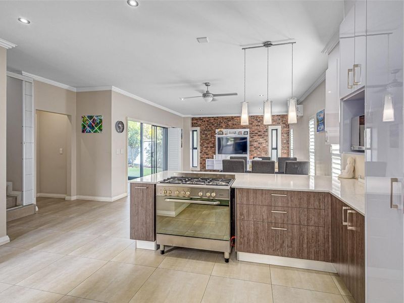Spacious open-plan kitchen and living area featuring modern cabinetry, stone countertops, a gas stove, and an exposed brick feature wall with tiled flooring throughout.