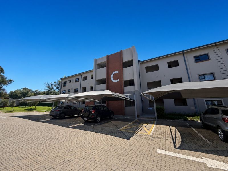 Exterior view of a multi-story apartment building featuring a paved parking area with shade cloth carports.