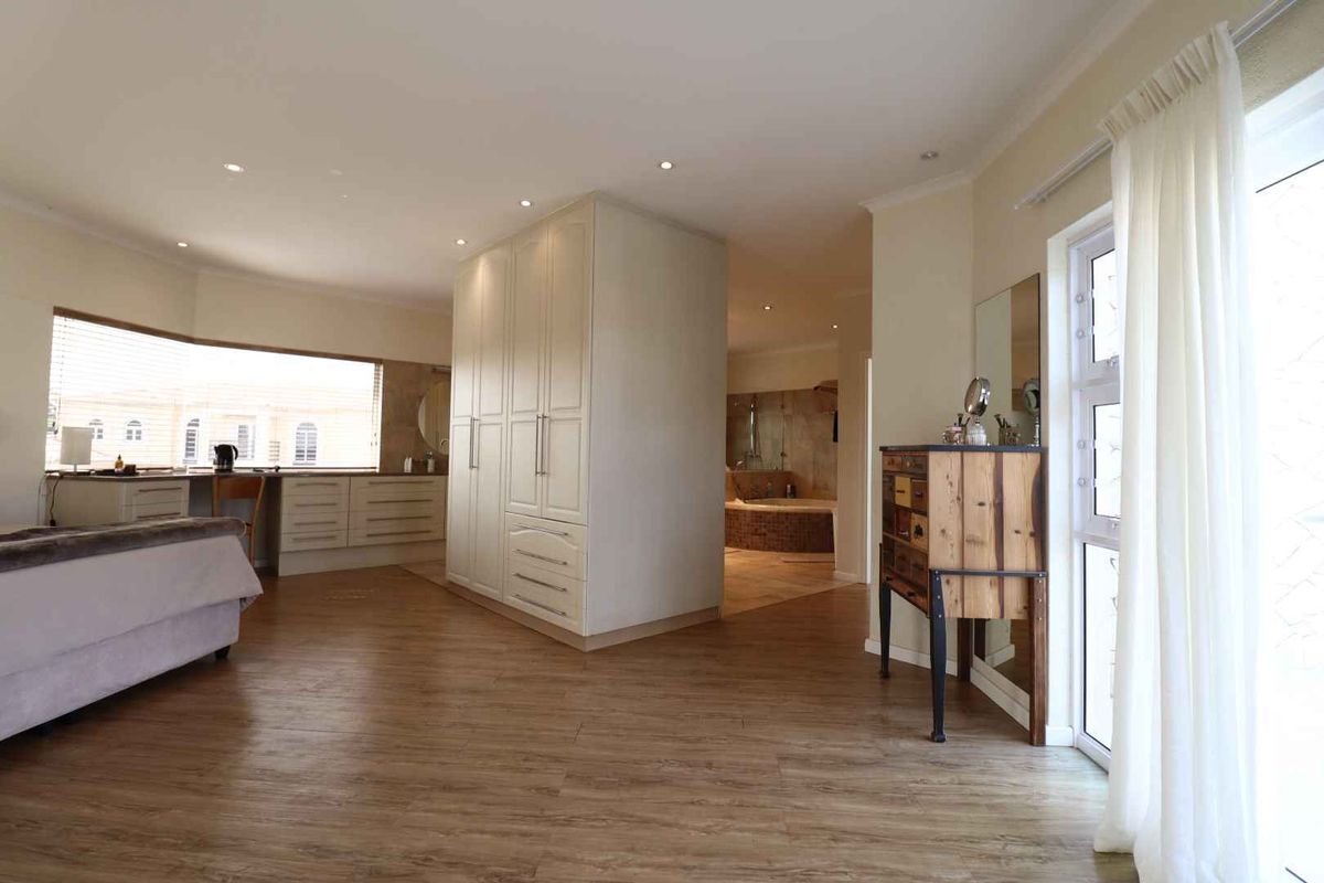 Spacious bedroom featuring built-in cabinetry, wood-look flooring, and an open-plan layout leading to an en-suite bathroom area with a soaking tub.