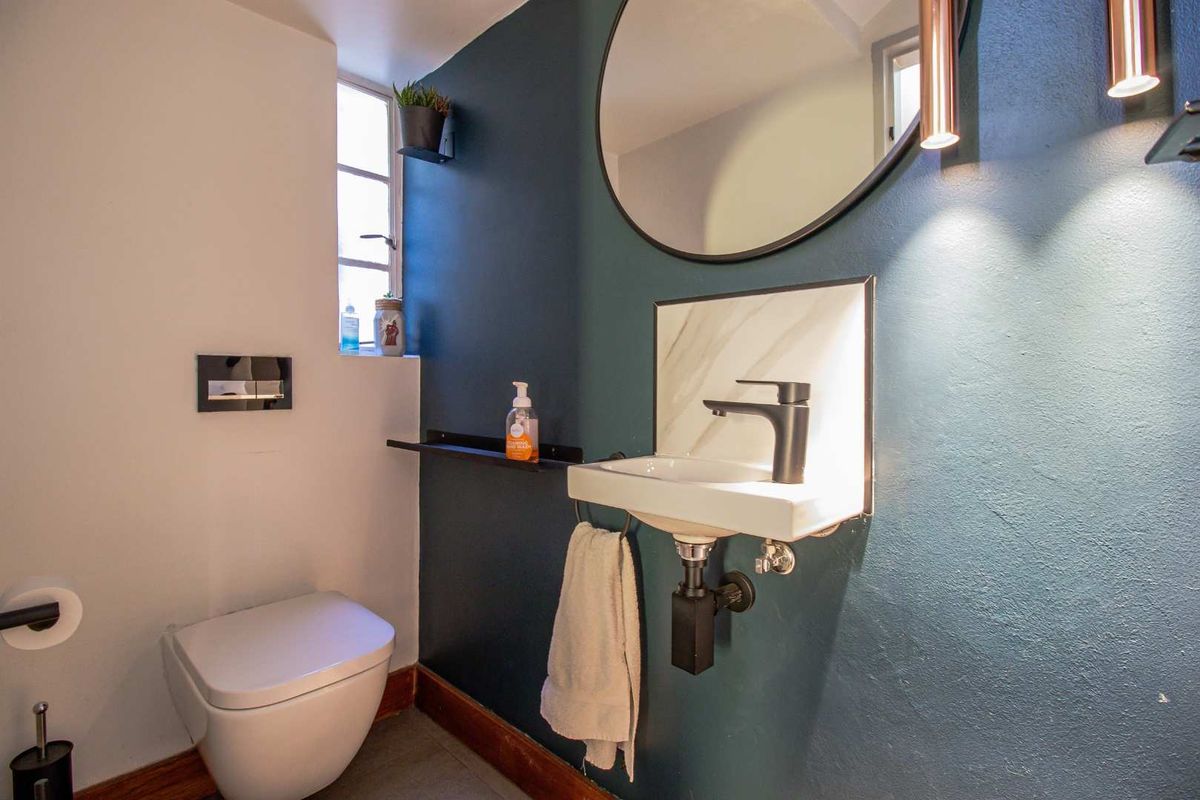 A modern guest bathroom featuring a wall-mounted toilet, a sleek marble-look vanity basin with matte black fixtures, and a bold dark blue accent wall.
