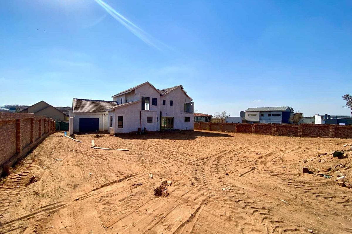 Rear view of a residential property under construction, featuring a large undeveloped plot, brick boundary walls, and a partially completed house structure.