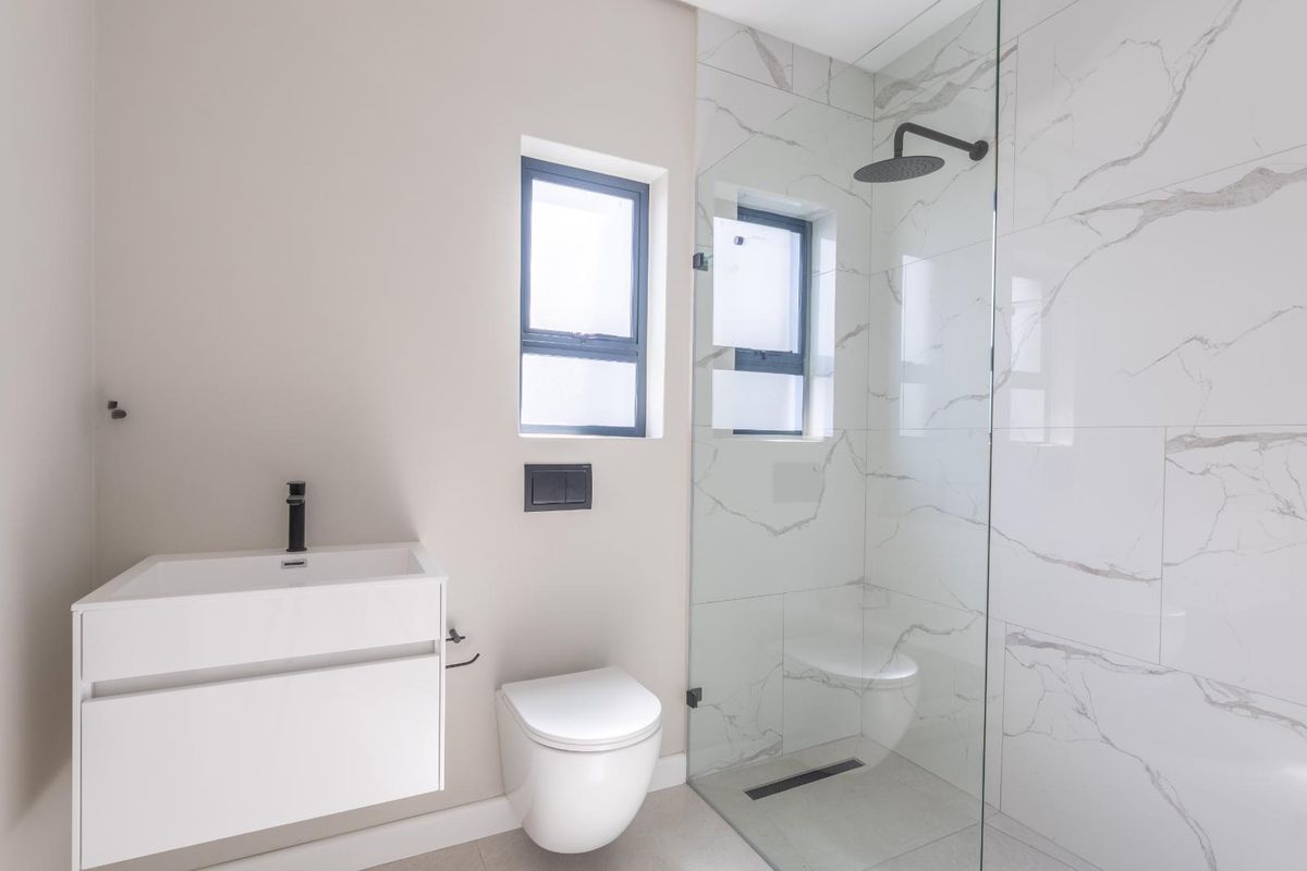 Modern bathroom featuring a wall-mounted vanity, wall-hung toilet, and a spacious walk-in shower with marble-look tiling and contemporary black fixtures.