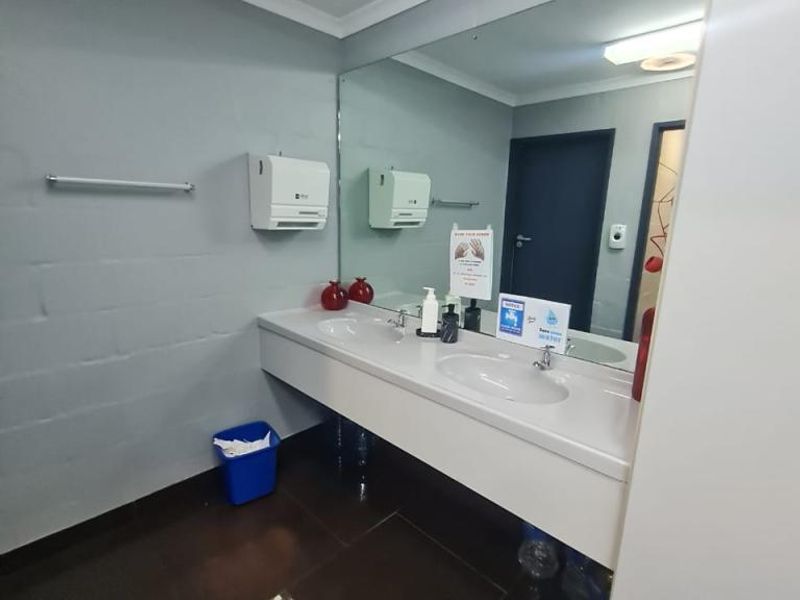 A clean and functional office bathroom featuring a double vanity with a large wall mirror and tiled flooring.