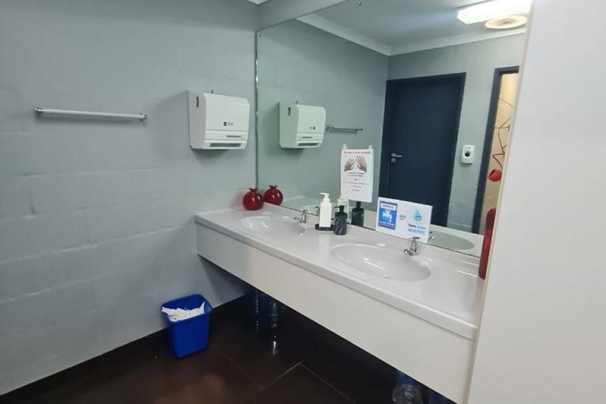 A clean and functional office bathroom featuring a double vanity with a large wall mirror and tiled flooring.