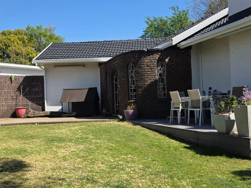A rear view of the property featuring a well-maintained lawn, a wooden deck area, and secure perimeter fencing.