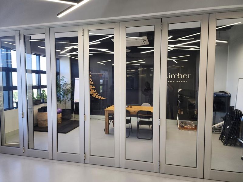 Modern office space featuring high-quality bi-fold glass partition doors, contemporary linear lighting, and a bright, professional atmosphere.