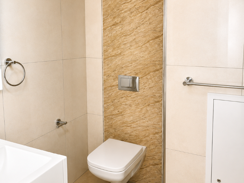 A modern, clean bathroom featuring a wall-mounted toilet with a concealed cistern, chrome fixtures, and neutral-toned ceramic tiling throughout.