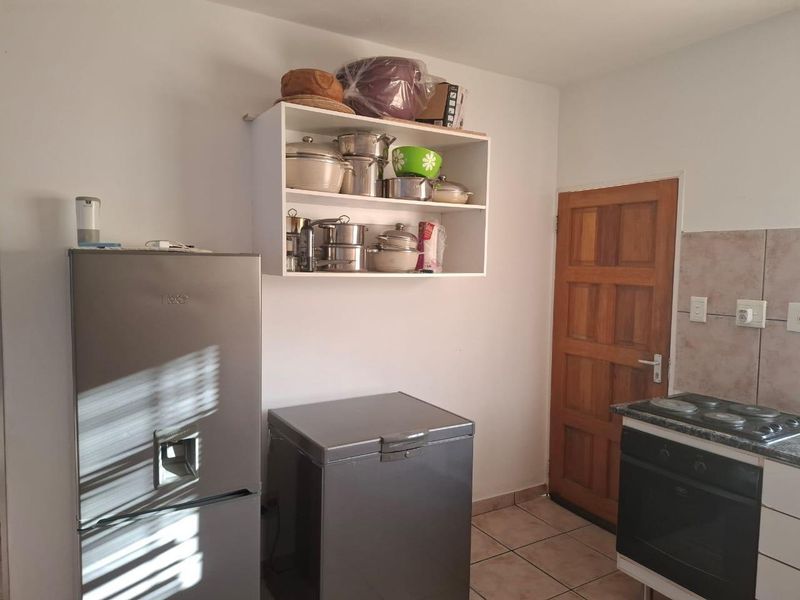 A functional kitchen area featuring tiled flooring, a built-in oven with hob, tiled splashback, and wall-mounted storage shelving.
