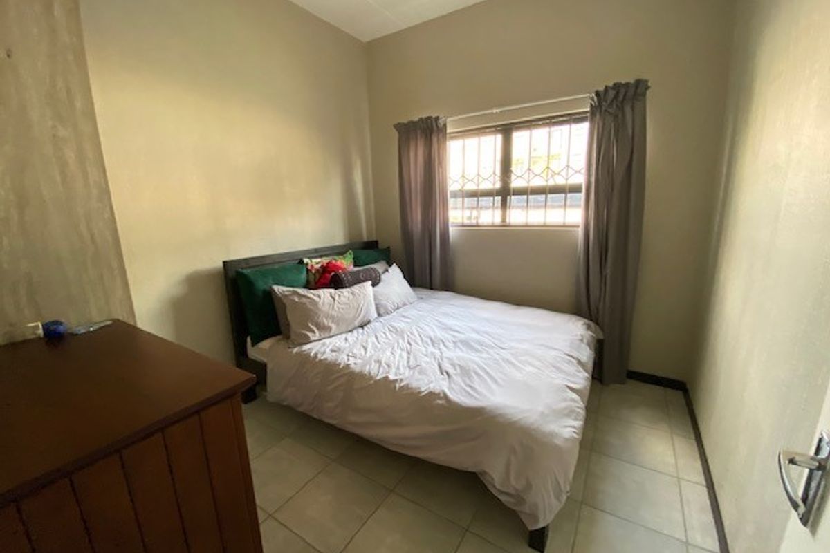 A functional bedroom featuring tiled flooring and a window fitted with security bars, providing a simple and practical living space.