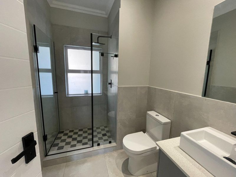 Modern bathroom featuring a glass-enclosed shower, contemporary vanity with stone countertop, and neutral tiled finishes throughout.