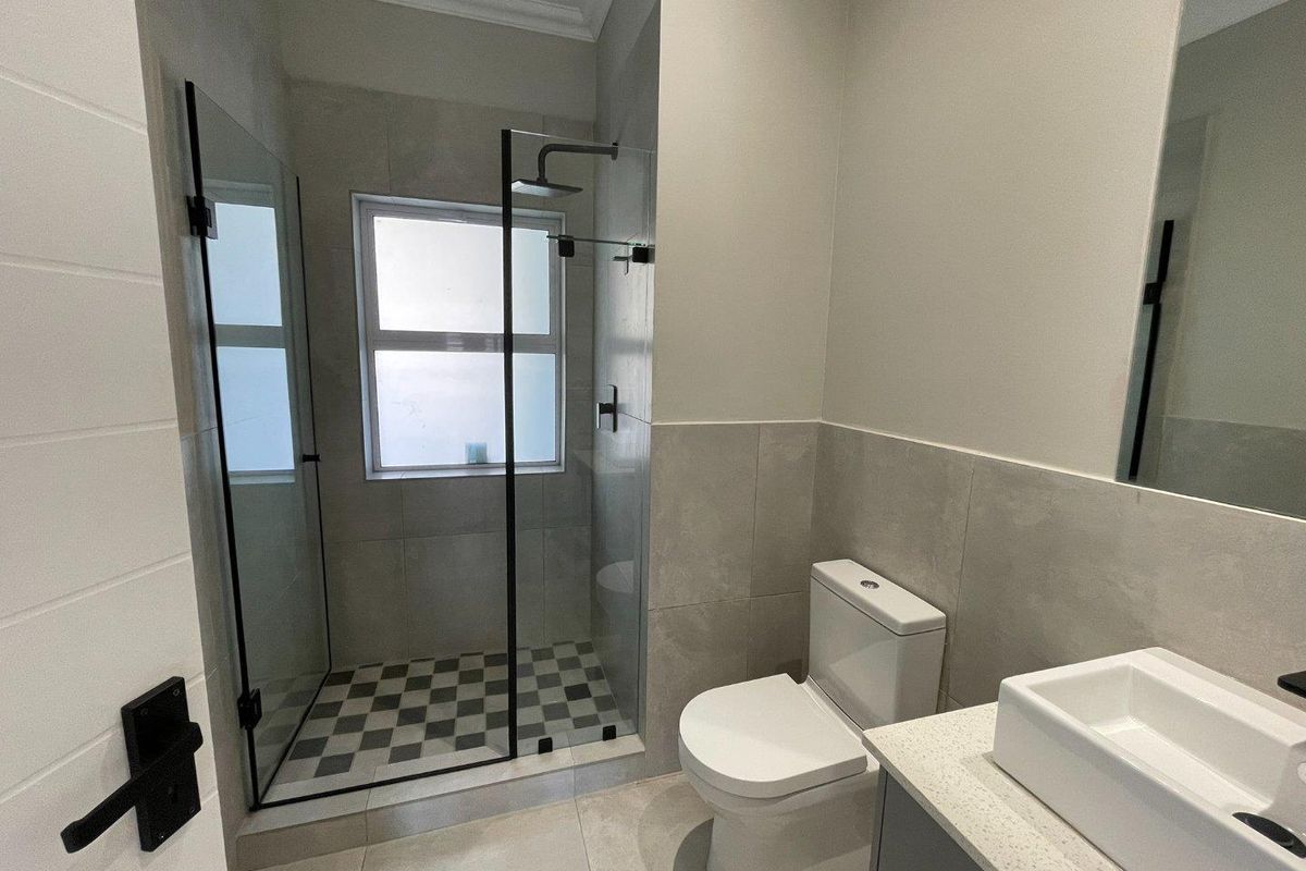 Modern bathroom featuring a glass-enclosed shower, contemporary vanity with stone countertop, and neutral tiled finishes throughout.