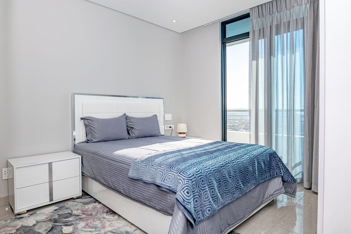 Modern bedroom featuring tiled flooring, recessed ceiling lighting, and a large glass sliding door providing access to a private balcony with scenic views.