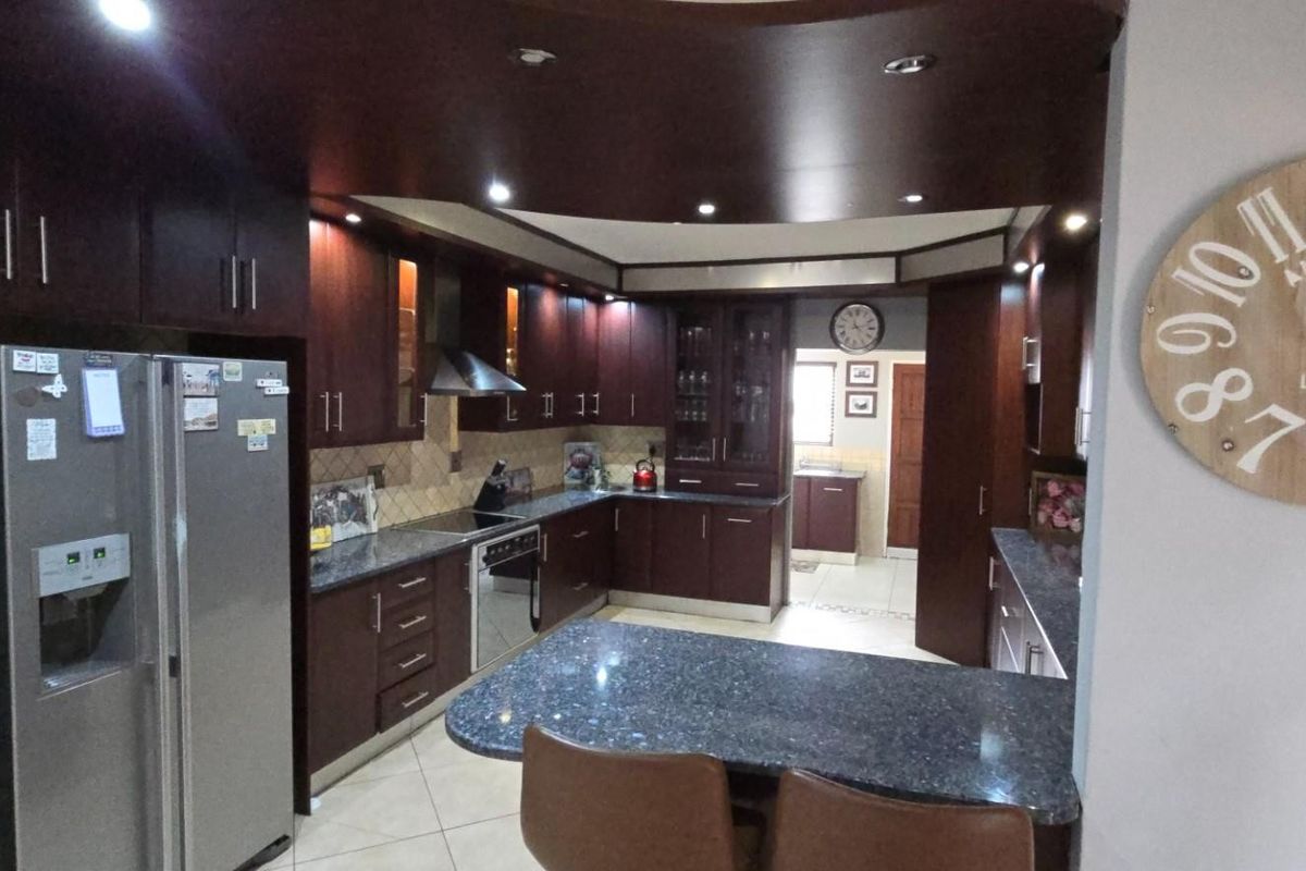 Spacious kitchen featuring dark wood cabinetry, granite countertops, integrated appliances, and recessed lighting, with an open-plan layout connecting to adjacent areas.