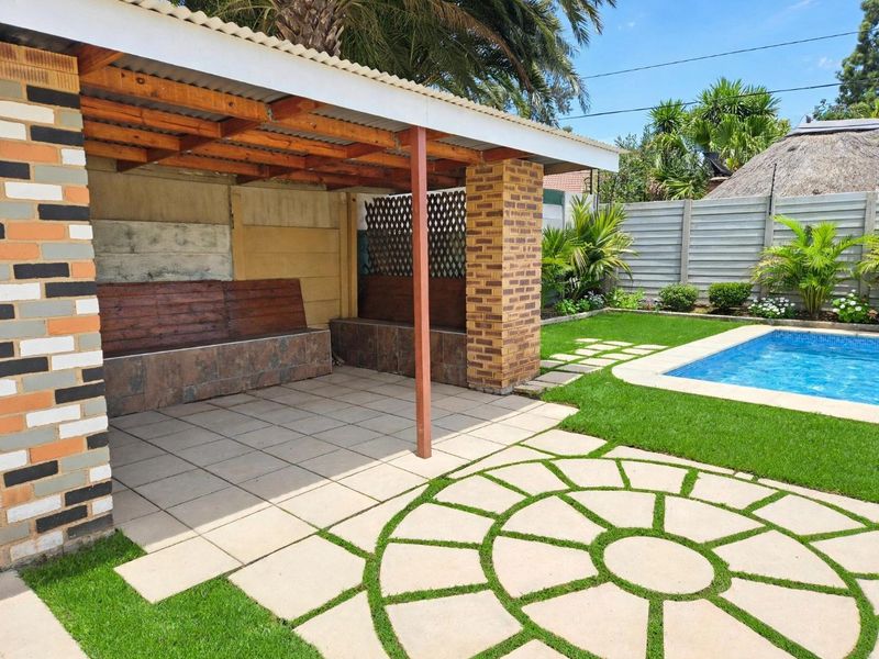 Outdoor covered patio area featuring built-in bench seating, tiled flooring, and direct access to a swimming pool and landscaped garden.