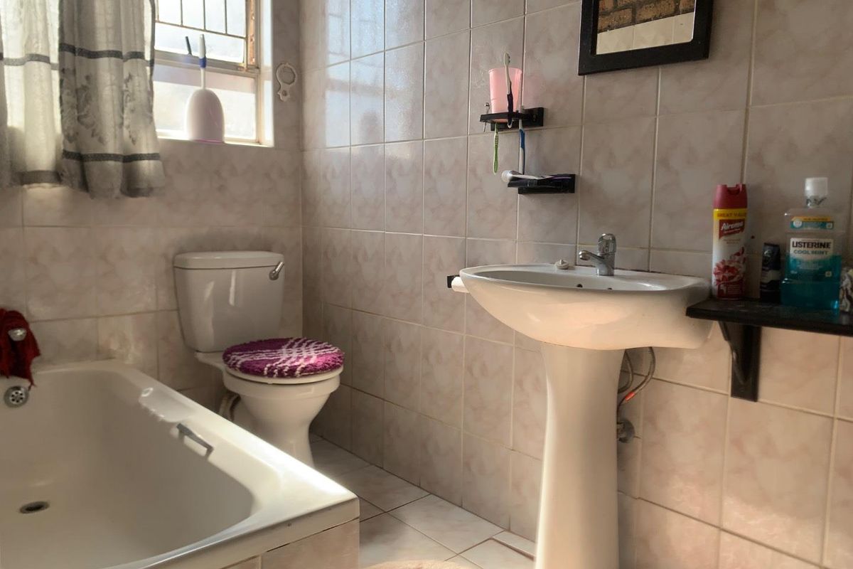A functional bathroom featuring a pedestal sink, a standard bathtub, and tiled walls with a window for natural light.