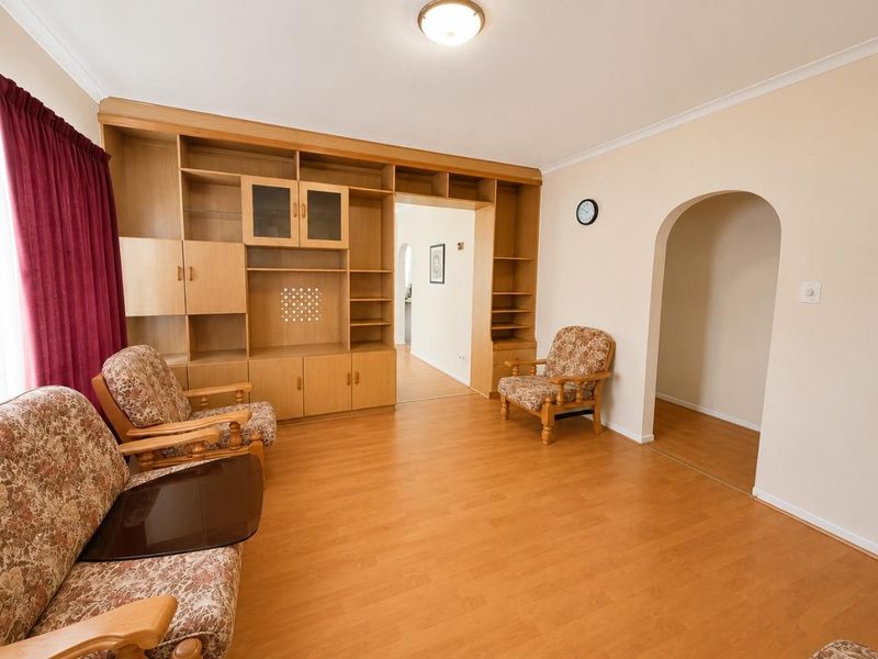 A living room featuring laminate flooring, a large built-in wooden wall unit, and an arched doorway leading to an adjacent space.