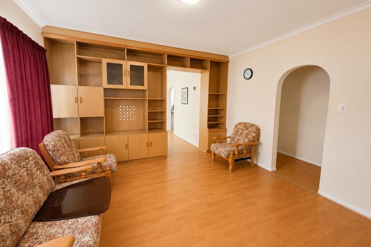 A living room featuring laminate flooring, a large built-in wooden wall unit, and an arched doorway leading to an adjacent space.