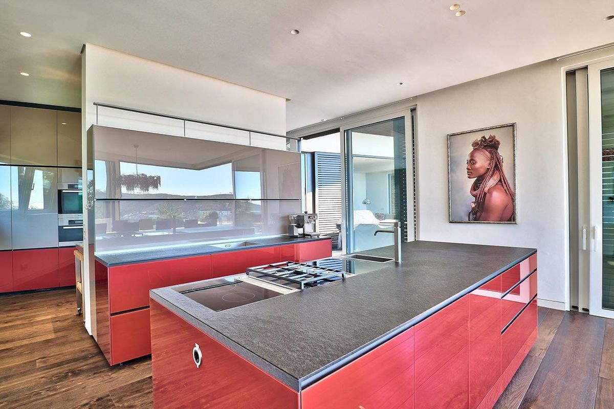 Modern kitchen featuring a large island with integrated gas and electric hobs, high-gloss red cabinetry, stone countertops, and seamless access to outdoor living areas.