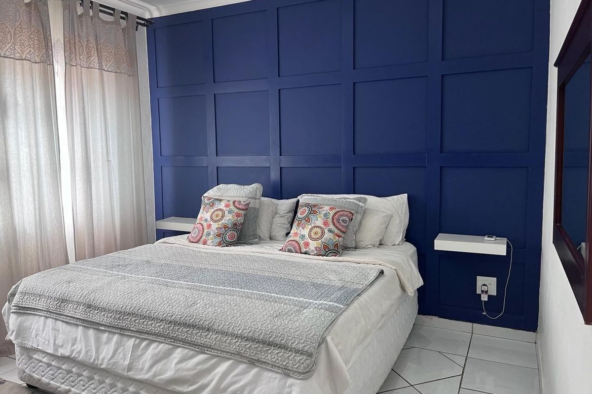 A bedroom featuring a bold blue accent wall with decorative wainscoting, wall-mounted bedside shelves, and tiled flooring.
