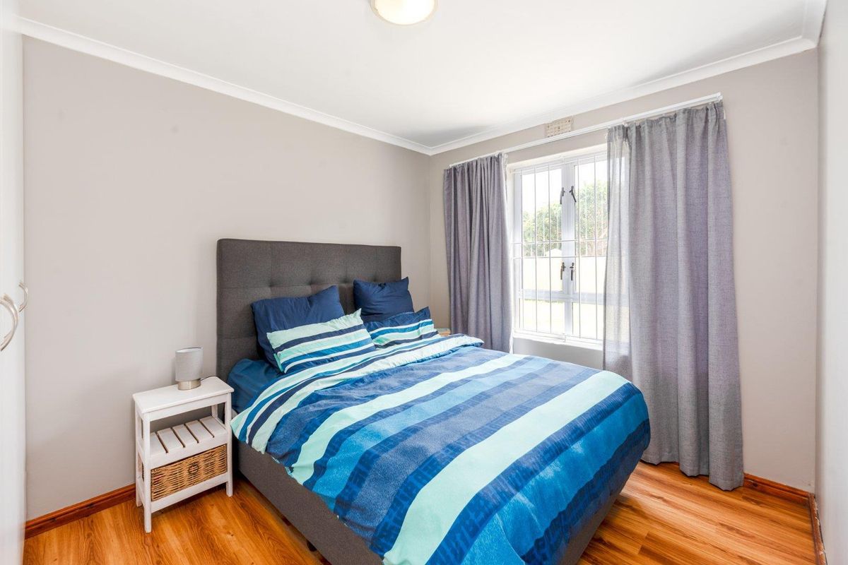 A well-lit bedroom featuring laminate wood flooring, neutral wall paint, and a window with security bars.