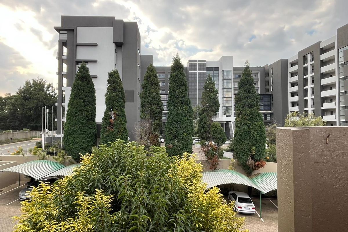 View of the apartment complex exterior featuring modern multi-story architecture, landscaped grounds, and covered parking facilities.