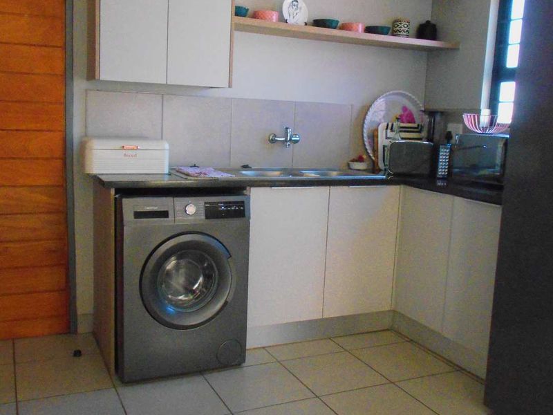 A functional laundry area featuring built-in cabinetry, open shelving, a stainless steel sink, and tiled flooring.