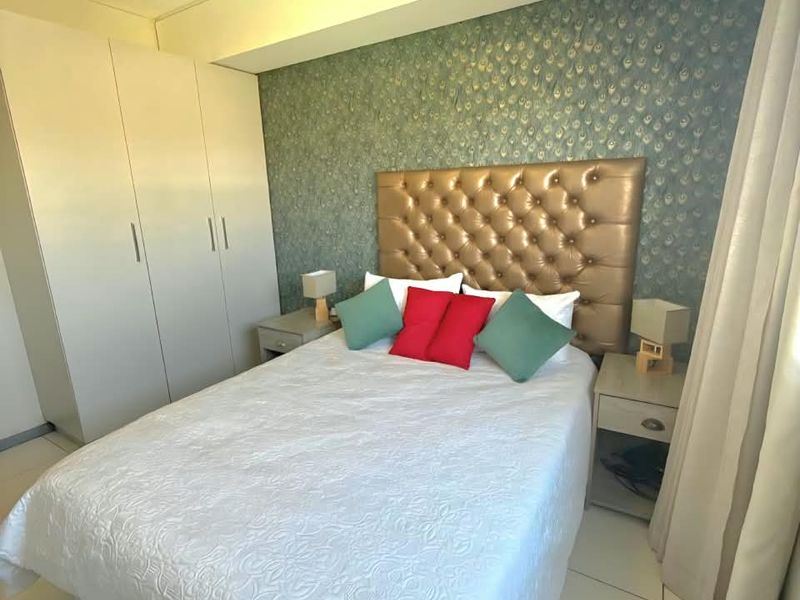 A well-maintained bedroom featuring built-in wardrobes, tiled flooring, and a decorative feature wall.