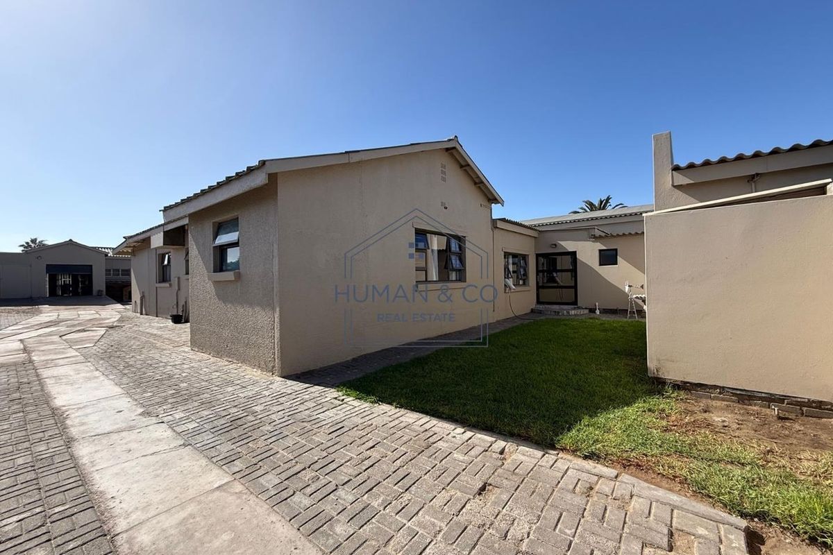 Exterior view of the property featuring a paved driveway, small lawn area, and single-story building structure with tiled roofing.