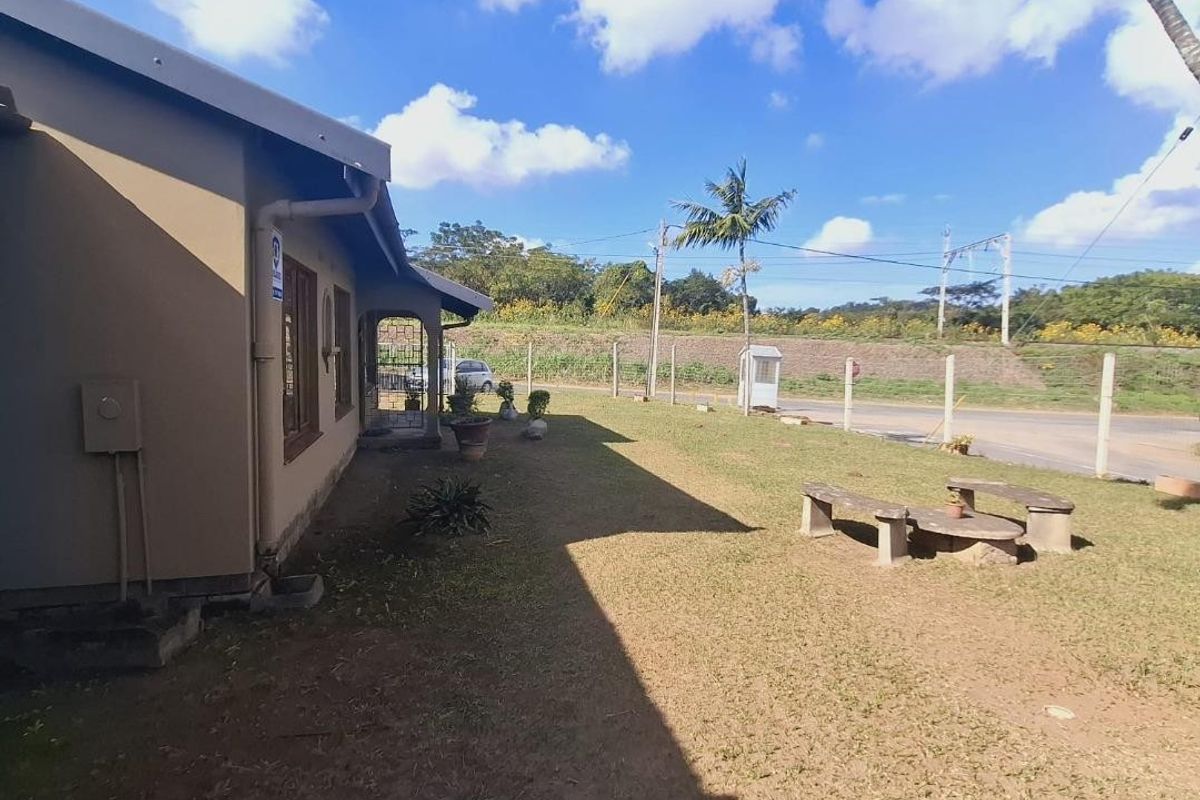 Rear exterior view of the property featuring a lawn area, perimeter fencing, and guttering along the building facade.