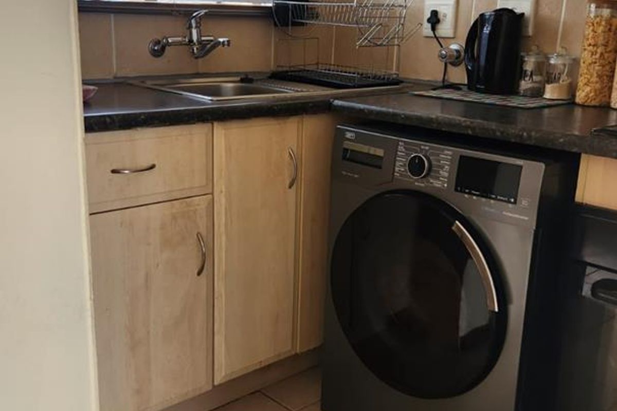 Compact kitchen area featuring light wood cabinetry, dark laminate countertops, tiled flooring, and a dedicated space for a front-loading washing machine.