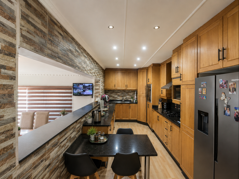 A well-maintained kitchen featuring warm wooden cabinetry, granite countertops, built-in appliances, and a breakfast bar overlooking the adjacent living area.