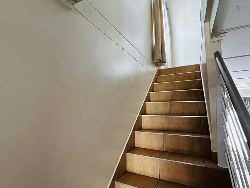 A staircase featuring tiled steps and a metal handrail, leading to an upper level landing.