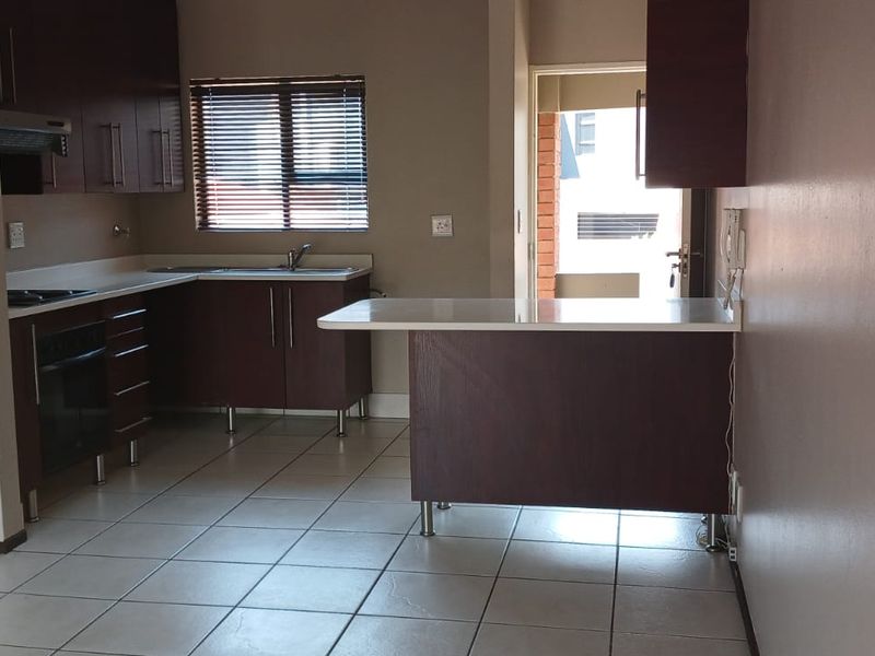 A functional kitchen featuring dark wood cabinetry, laminate countertops, a breakfast bar, and tiled flooring, with direct access to an outdoor area.