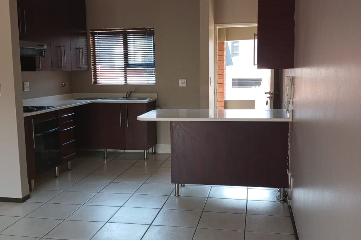 A functional kitchen featuring dark wood cabinetry, laminate countertops, a breakfast bar, and tiled flooring, with direct access to an outdoor area.