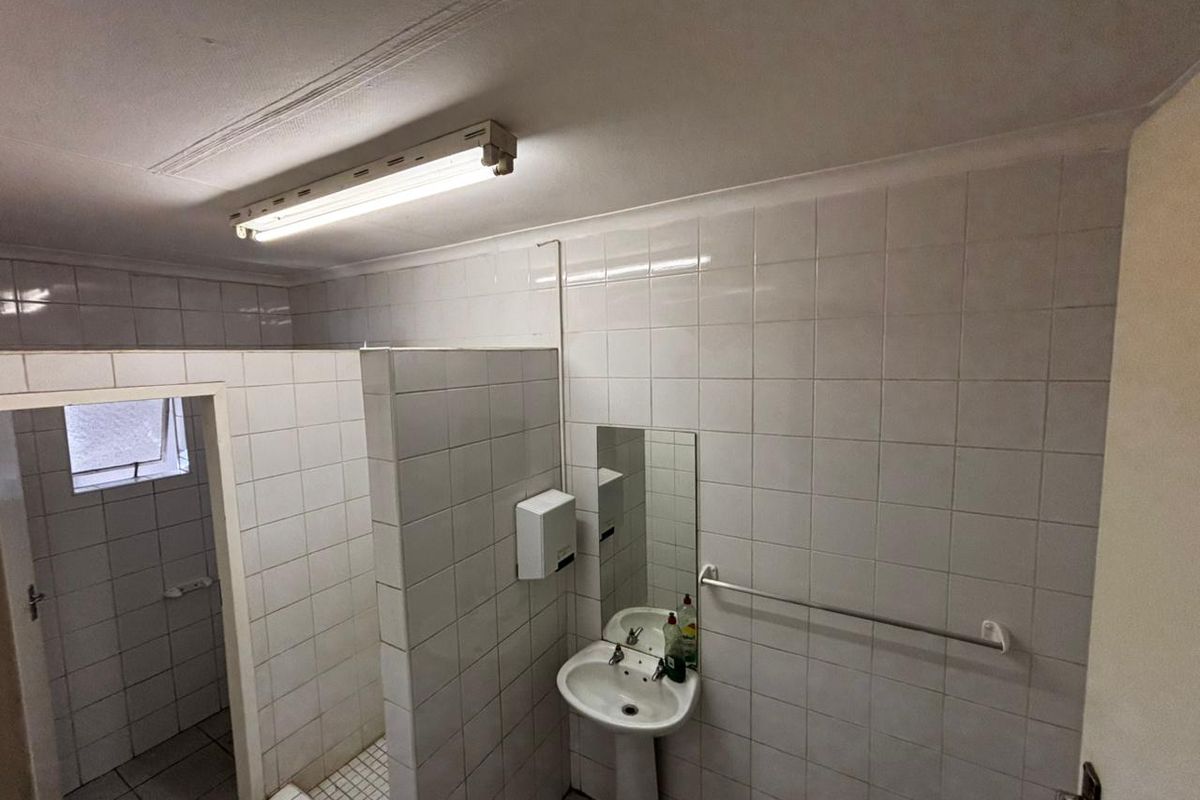 Functional commercial bathroom featuring tiled walls and flooring, a pedestal basin, and a partition wall for privacy.
