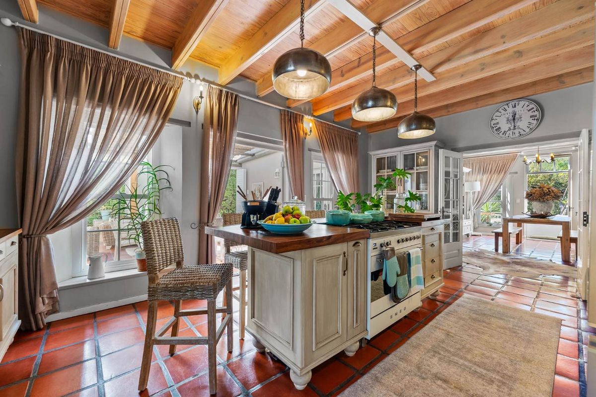 A charming kitchen featuring exposed timber ceiling beams, terracotta floor tiles, a central island with a butcher block countertop, and a classic Smeg range cooker.