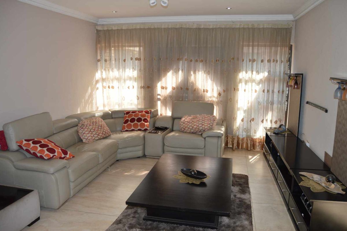 A comfortable living room featuring tiled flooring, recessed ceiling lighting, and large windows dressed with sheer curtains, providing a bright and inviting atmosphere.
