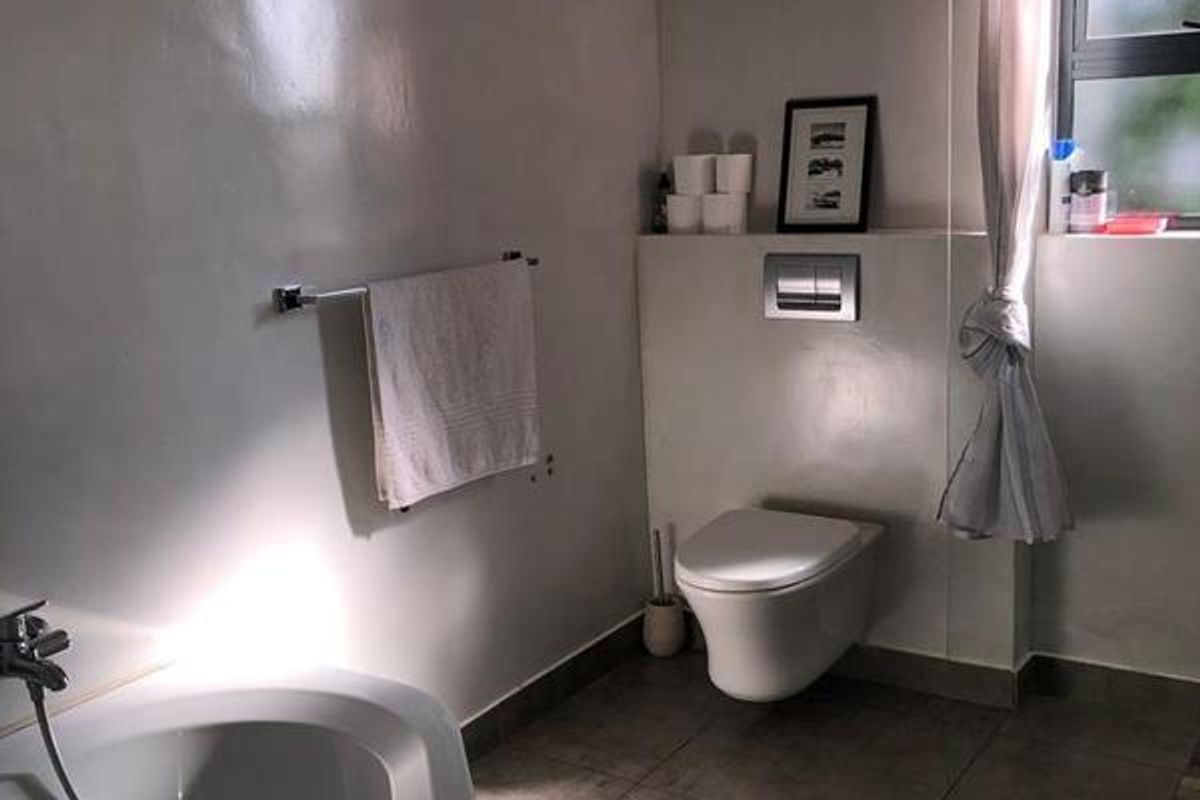 A functional bathroom featuring a wall-mounted toilet with a concealed cistern, a bathtub, and tiled flooring.