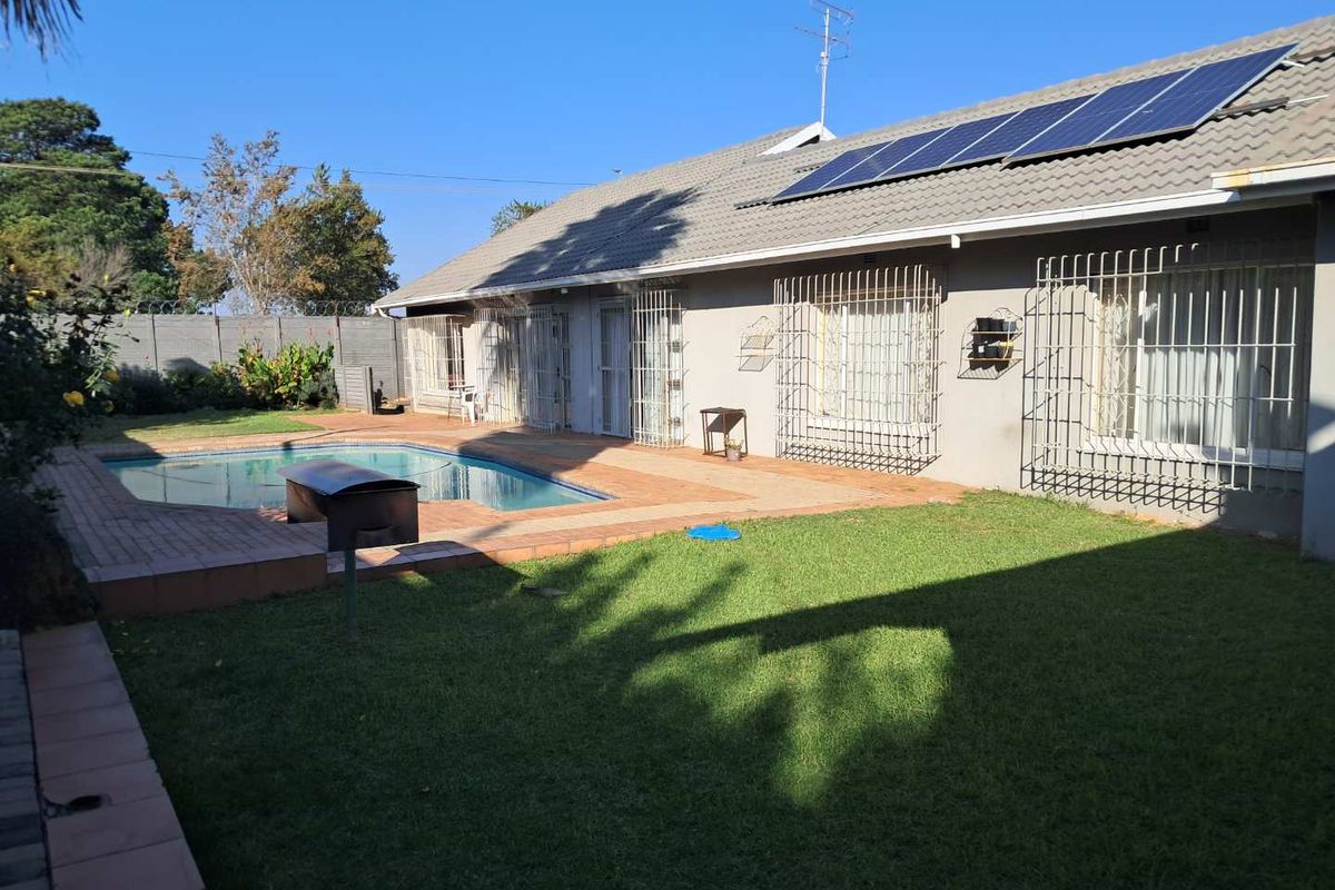 Rear view of the property featuring a swimming pool, paved patio area, and a well-maintained lawn with roof-mounted solar panels.