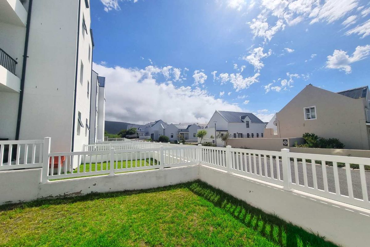 A view of the exterior garden area featuring a white picket fence, manicured lawn, and surrounding residential apartment building architecture.