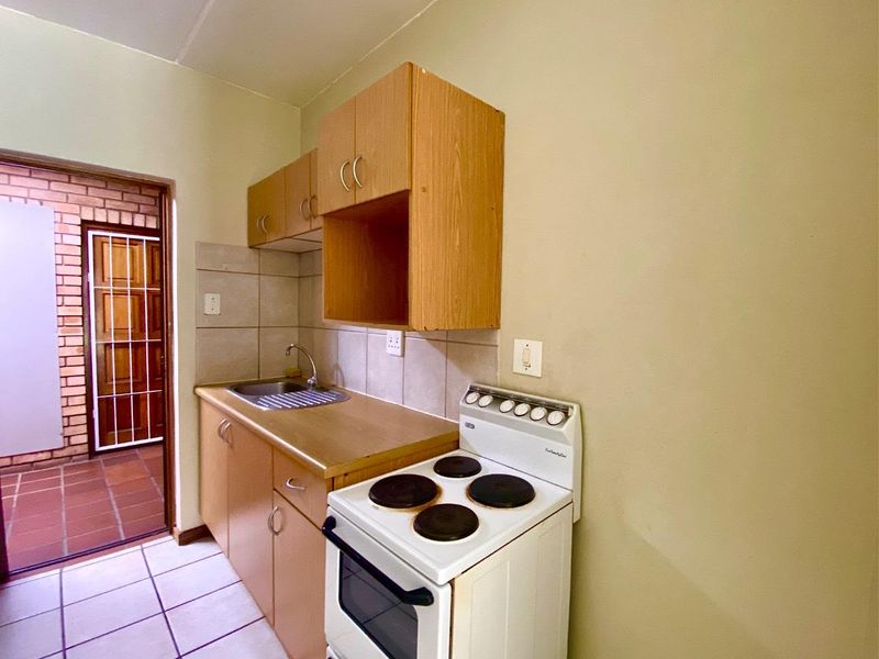 Compact kitchen featuring laminate cabinetry, a stainless steel sink, tiled backsplash, and a freestanding electric stove, with direct access to an outdoor area.