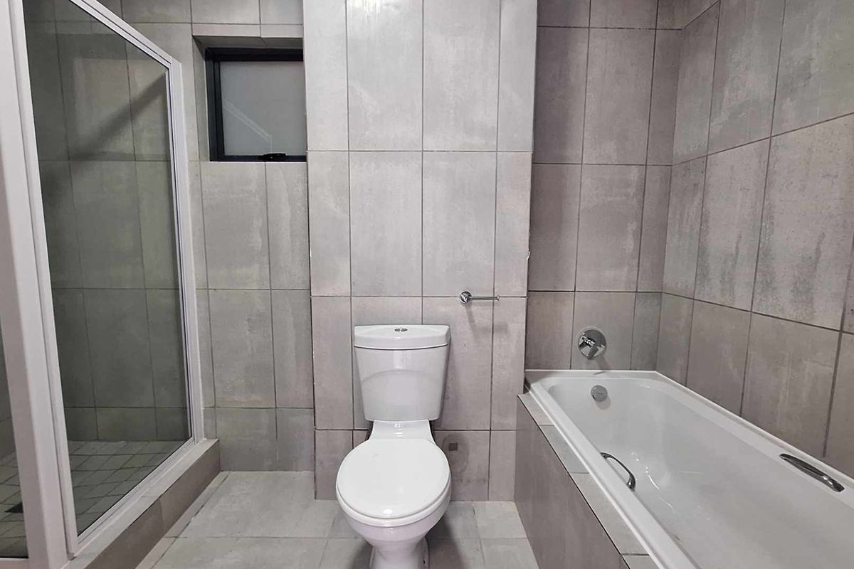 A modern, neutral-toned bathroom featuring a glass-enclosed shower, a built-in bathtub, and a standard toilet with full-height wall tiling.