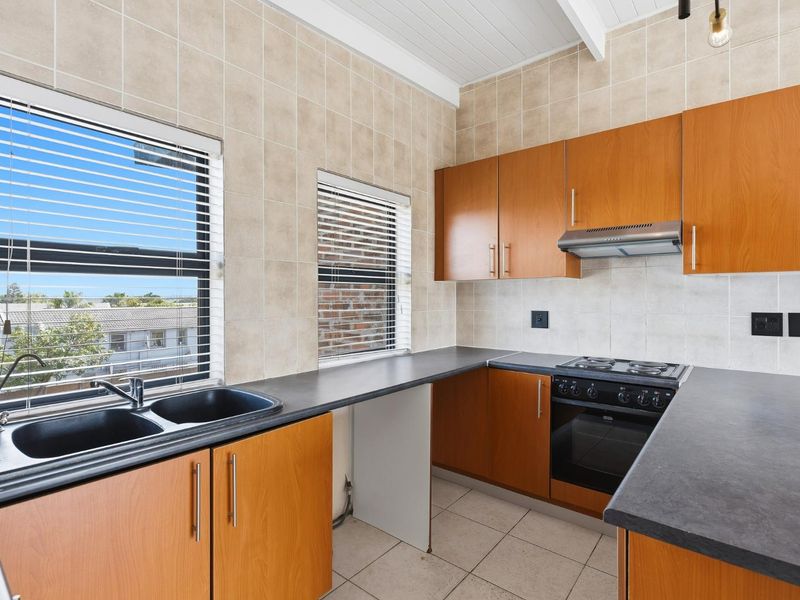 A functional kitchen featuring wood-look cabinetry, dark countertops, a built-in oven with gas hob, and tiled finishes throughout.