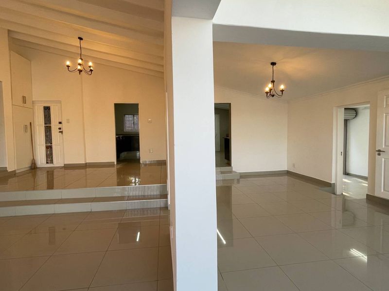 Spacious open-plan living area featuring large format floor tiles, a vaulted ceiling, and a raised platform section, offering a bright and versatile layout.