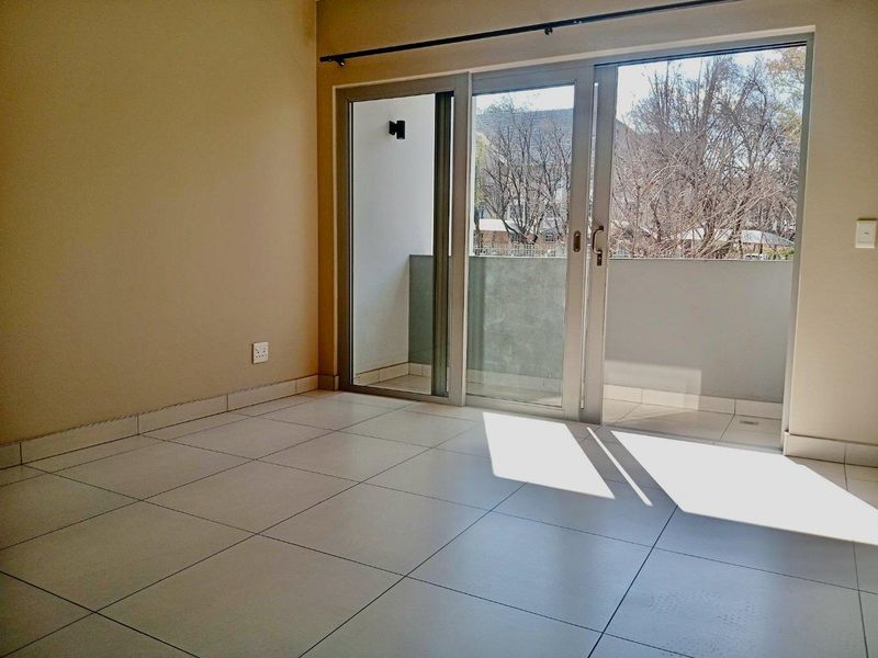 A bright, empty living area featuring neutral tiled flooring and large sliding glass doors that provide direct access to a private balcony.